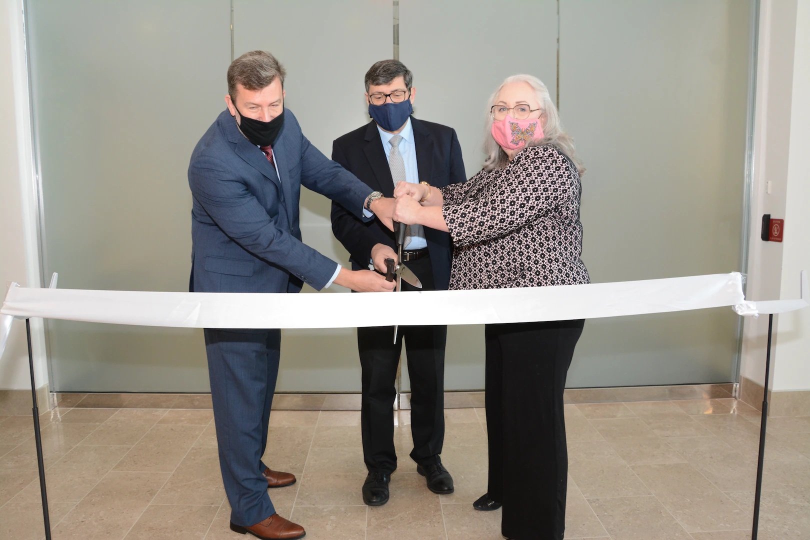 Photo of three people cutting a ribbon in front of a new office.
